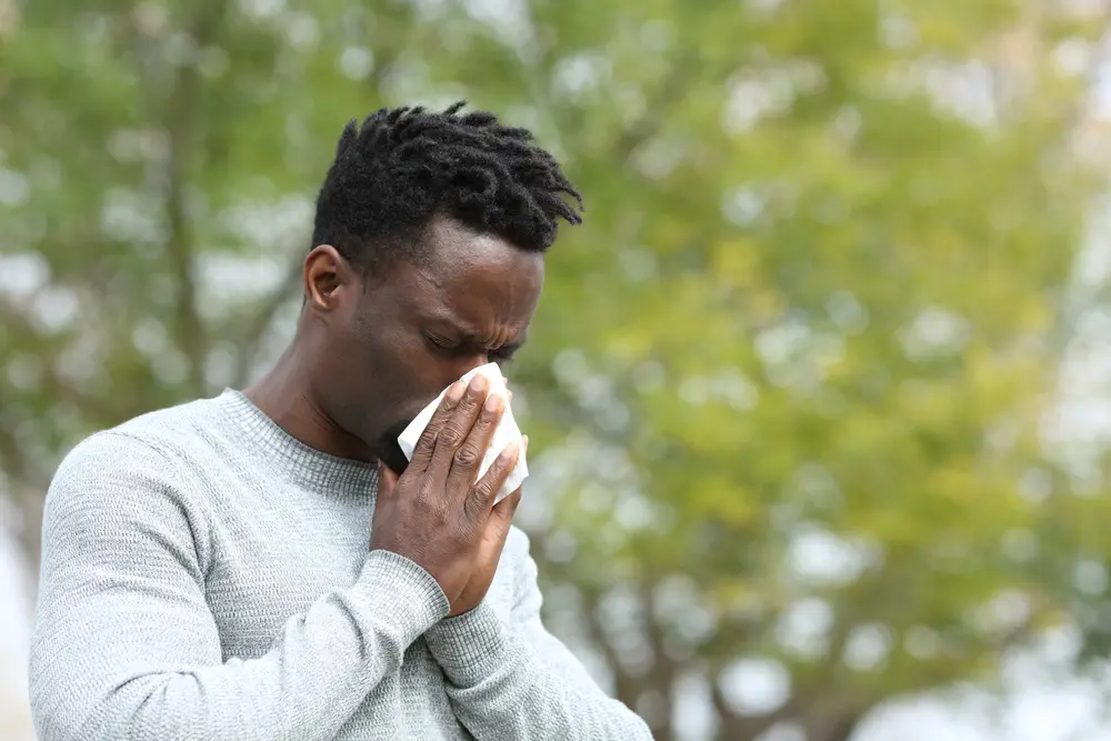 man blowing nose in tissue outside.