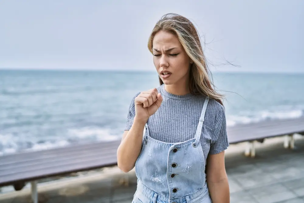 Woman with a sore throat standing on the beach.